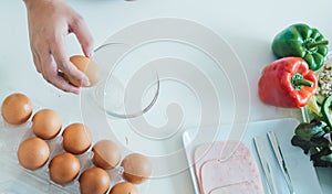 Woman cracking an egg into a bowl with standing by in kitchen.