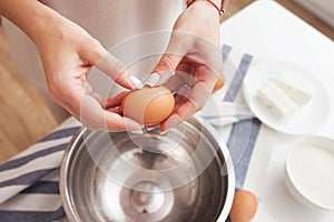 Woman cracking eggs into bowl. Hands holding egg