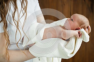 A woman cradles a newborn in a white blanket with a comforting gesture