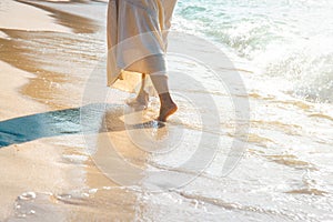 Woman in a cream dress is walking, enjoying on the beach.