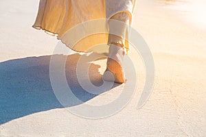 Woman in a cream dress is walking, enjoying on the beach at suns