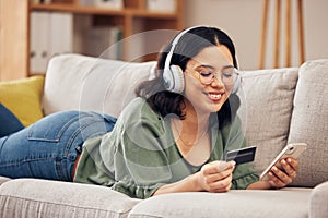 Woman, credit card and phone on sofa, home and headphones with smile, online shopping or payment on web. Girl