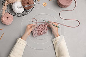 Woman crocheting with threads at grey table, top view. Engaging hobby