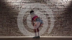 Woman in the crop top and denim shorts dance twerk against a brick wall. Slow motion