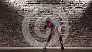 Woman in crop top and denim shorts dance twerk against a brick wall. Slow motion