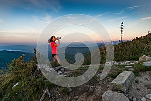 Woman cross country runner drinking water in mountains at summer