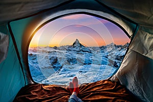 Woman cross leg on blanket in camping tent with sleeping bags on mountain hill. view from inside with Matterhorn mountains