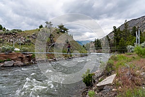 Woman Crosses Footbridge Over Rushing Water