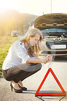 Woman crouching on the road. Sad person. Damaged car. Natural background. Car accident.
