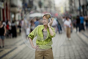 A woman is on a crowded street. She is listening to music on her headphones.