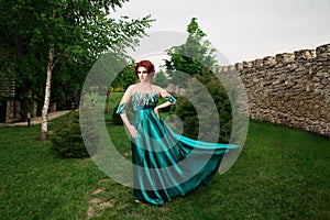 Woman with crown on head in green long dress posing looking to side