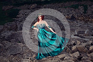 Woman with crown on head in green long dress posing looking to side