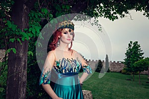 Woman with crown on head in green long dress posing looking at you camera