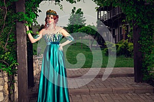 Woman with crown on head in green long dress posing looking at you camera