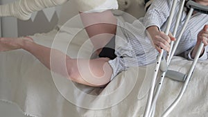 A woman on crutches in plaster on her leg to lie on the bed at home