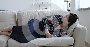 Woman crying lying on couch curled up due menstrual cramps