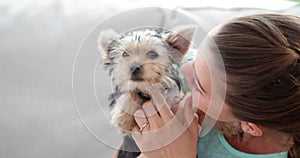 Woman cuddling her cute yorkshire terrier puppy on sofa