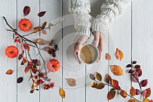 Woman with cup of coffee, leaves, small pumpkins and rowan on white retro wood boards. background. Autumn, fall concept. Flat lay,