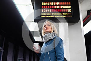 Woman with cup of coffee waiting for her train on platform of railway station