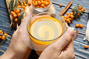 Woman with cup of fresh sea buckthorn tea at blue wooden table, closeup