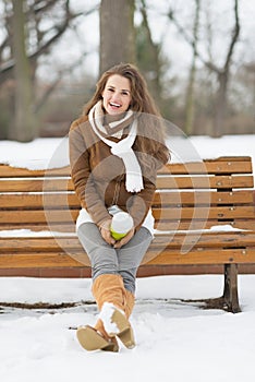 Woman with cup of hot beverage sitting on bench in winter park