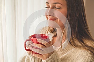 Woman with cup of hot drink by the window. Looking at window and drink tea. Good morning with tea.