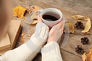 Woman with cup of hot drink at wooden table, closeup. Cozy autumn atmosphere