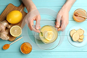 Woman with cup of immunity boosting drink at turquoise wooden table, top view
