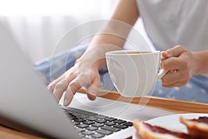 Woman with cup of morning coffee working on laptop, closeup