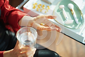 Woman with cup of water taking pill near table with toiletries