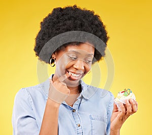 Woman, cupcake and studio with thinking, diet and temptation for guilt with junk food by yellow background. African