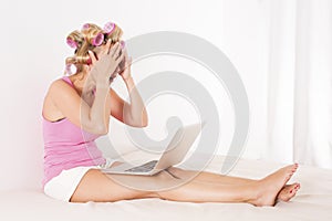 Woman with curlers in bed with laptop