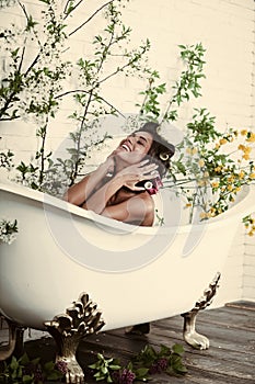 Woman with curlers on hair sit in bath, body care.