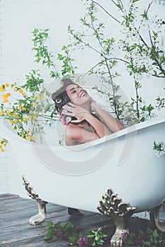 Woman with curlers on hair sit in bath, body care.