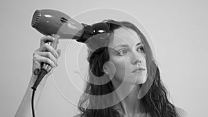 A woman with curly hair dries her hair with a hair dryer with a diffuser attachment. Black and white photo