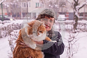 Žena s kučeravými vlasmi drží oranžovú mačku v zasneženom dni