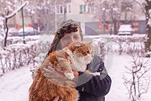 Woman with curly hair holding an orange cat in a snowy day