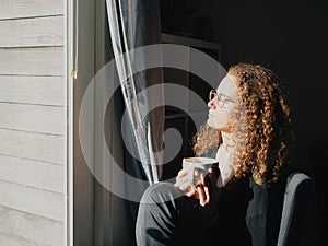 A woman with curly hair is sitting in a chair with a cup of tea enjoying the sun