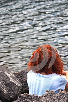 A woman with curly hair is sitting in front of the sea