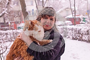 Woman with curly hair smiling and holding an orange cat in a snowy day