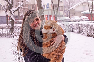 Woman with curly hair smiling and holding an orange furry cat in a snowy day