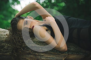 Woman with curly hairstyle in summer. Woman with long brunette hair relax on tree on nature. Hair care, therapy and