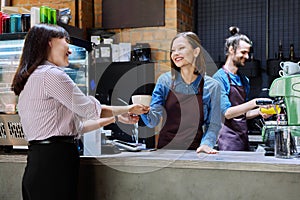 Woman customer of coffee shop near counter with cup of coffee talking to restaurant workers