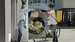 Woman customer open door to a food delivery man wearing yellow thermal backpack on a bike and receives order or package