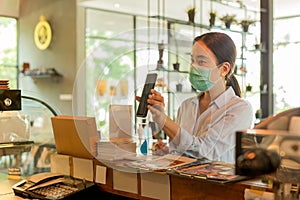Woman customer with protective mask paying bill by cell phone in cafe.