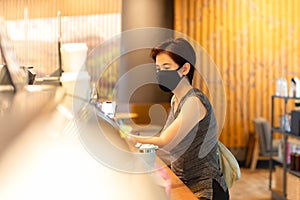 Woman customer with protective mask paying bill by cell phone in cafe.