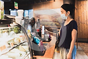 Woman customer with protective mask paying bill by cell phone in cafe.