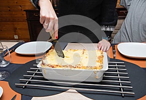 Woman cut with knife hot tasty home baking lasagna in ceramic casserole dish