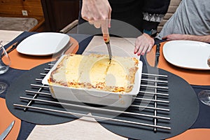 Woman cut with knife hot tasty home baking lasagna in ceramic casserole dish