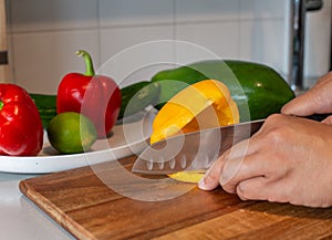 A woman cut yellow pepper on the wooden board in the kitchen